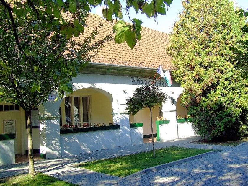 A kiskunlacházai községháza klasszicista, boltíves homlokzata fák és gyalogút mellett