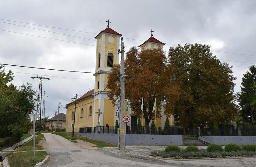 A polgárdi Szent István király templom sárga homlokzata két tornyával, fák között